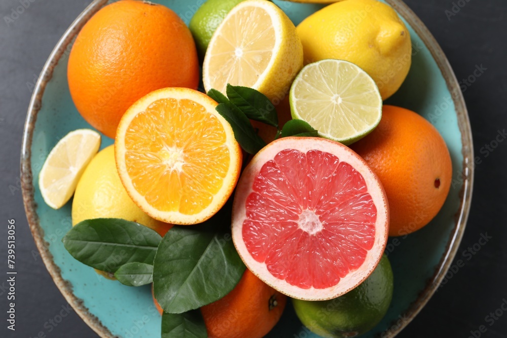 Different cut and whole citrus fruits on black table, top view