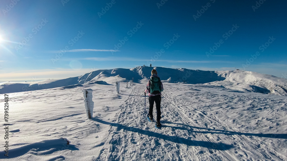 Woman in snowshoes on the way to majestic summit peak Grosser Speikogel in Kor Alps, Lavanttal Alps, Carinthia Styria, Austria. Winter wonderland in Austrian Alps. Idyllic ski touring hiking trail