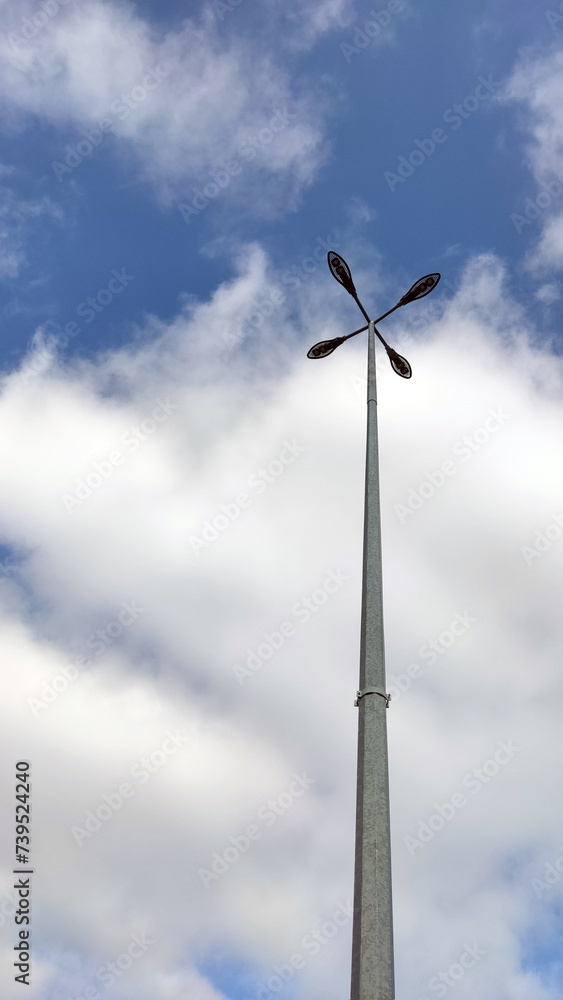 Lighting pole with four lamps against a background of cloudy sky in sunny weather. Urban electro-energy technologies. Savings on street urban lighting. Minimalism Lighting pole with four lamps against a background of cloudy sky in sunny weather. Urban electro-energy technologies. Savings on street urban lighting. Minimalism