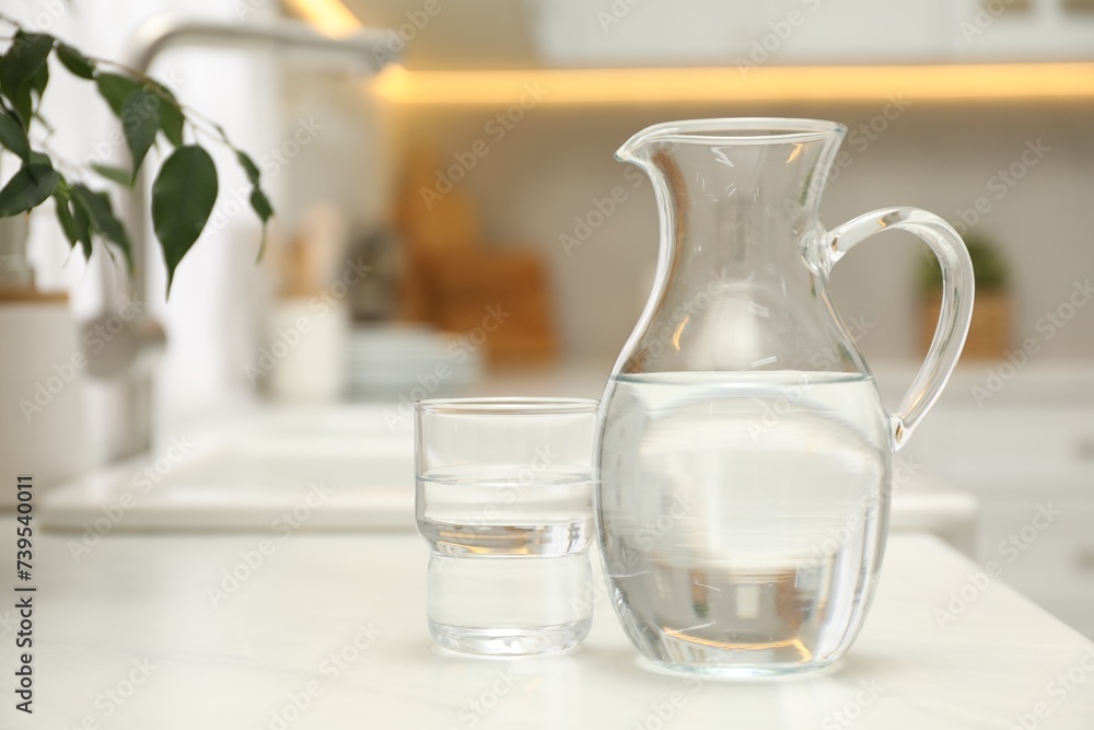 Jug and glass with clear water on white table in kitchen, space for text Jug and glass with clear water on white table in kitchen, space for text