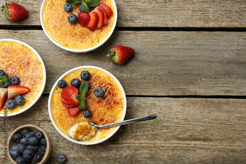 Flat lay composition with delicious creme brulee with berries and mint in bowls on wooden table. Space for text photo