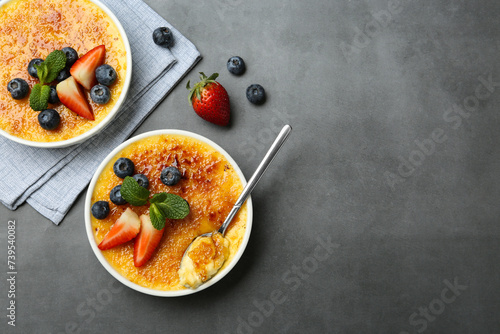 Delicious creme brulee with berries and mint in bowls on grey table, flat lay. Space for text photo