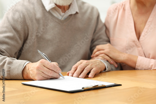 Senior couple signing Last Will and Testament at wooden table, closeup photo