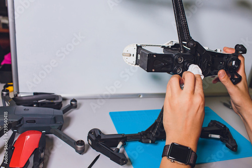 Closeup shot of man working on assembling new surveillance system using quadcopter drone with camera on table with different tools in modern workshop.