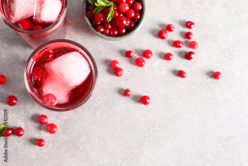 Tasty cranberry juice with ice cubes in glasses and fresh berries on light grey table, flat lay. Space for text