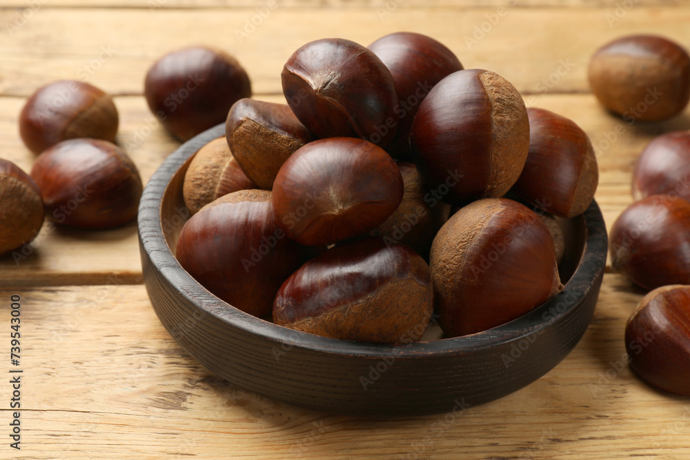 Sweet fresh edible chestnuts in bowl on wooden table, closeup Sweet fresh edible chestnuts in bowl on wooden table, closeup