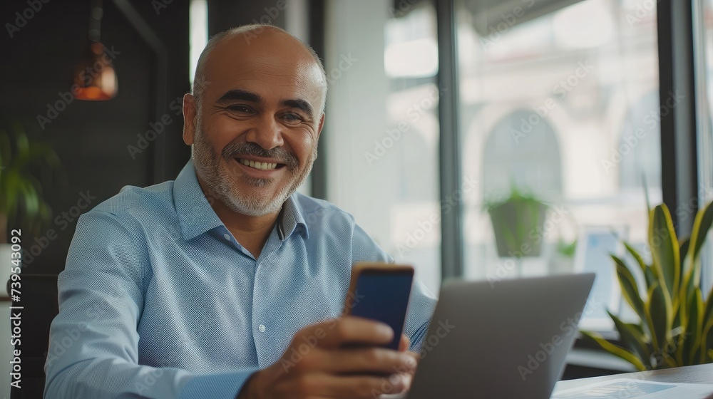 Middle aged Hispanic business manager ceo using cell phone mobile app, laptop. Smiling Latin or Indian mature man businessman holding smartphone sit in office working online on gadget with copy space. Middle aged Hispanic business manager ceo using cell phone mobile app, laptop. Smiling Latin or Indian mature man businessman holding smartphone sit in office working online on gadget with copy space.