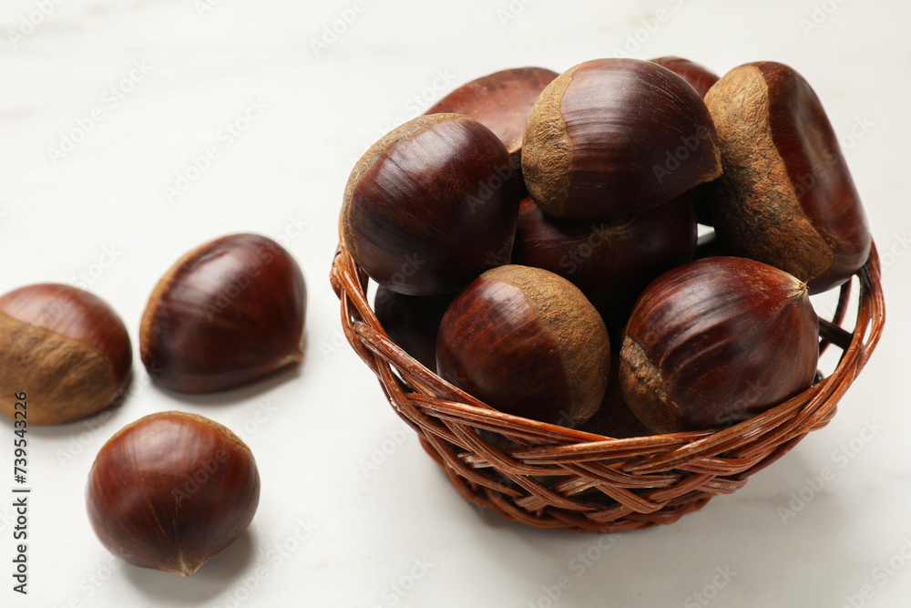 Sweet fresh edible chestnuts in wicker bowl on white table, closeup Sweet fresh edible chestnuts in wicker bowl on white table, closeup