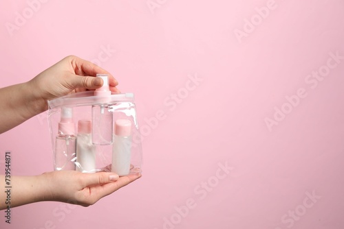 Cosmetic travel kit. Woman putting small bottle with personal care product into plastic bag against pink background, closeup. Space for text © New Africa