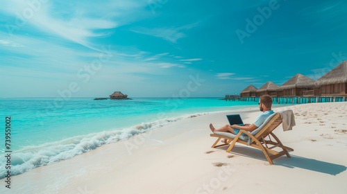 A man is working on a laptop while sitting in a deck chair on a tropical beach facing the ocean, with overwater bungalows in the background. Ai generative