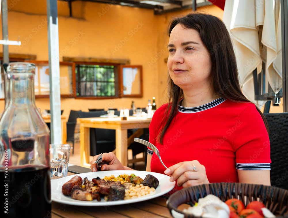Portrait of woman spending time on open terrace of catalan restaurant and eating traditional parillada de carne