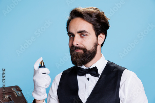 Rich elegant man spraying perfume, posing with bottle of luxurious cologne and indicating strong masculine scent. Young adult applying fresh fragrance to smell good, hotel concierge employee. photo