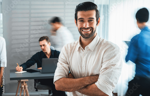 Confidence and happy smiling businessman portrait with blur motion background of his colleague and business team working in office. Office worker teamwork and positive workplace concept. Prudent
