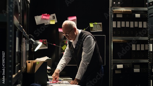 Police officer examining information on files classified records, reading witness statements to build case against culprit. Detective evaluating fingerprints and evidence authenticity. Tripod shot.