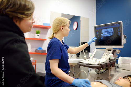 Doctor making abdominal ultrasound for boy using scanner machine. Doc runs ultrasound sensor over patient tummy looking at screen. Mother supports son during examination of internal organs