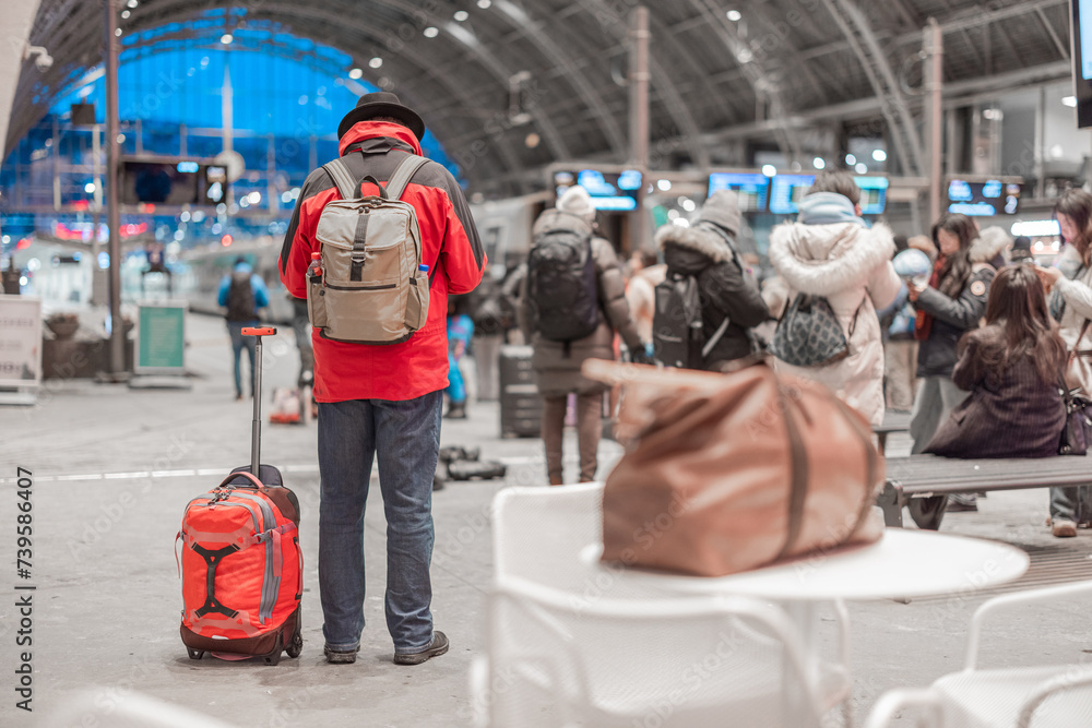 Unknown person with red jacket, backpack and a bag is waiting for a departure of a train in Bergen train station. Magnificent metal structure as a roof of a station.