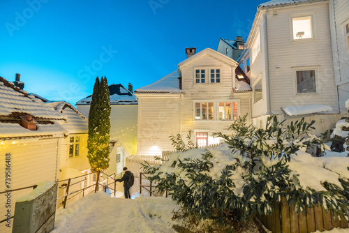 Unknown person descending through the narrow and steep streets of Bergen at night. Beaufiful white houses covered with snow.