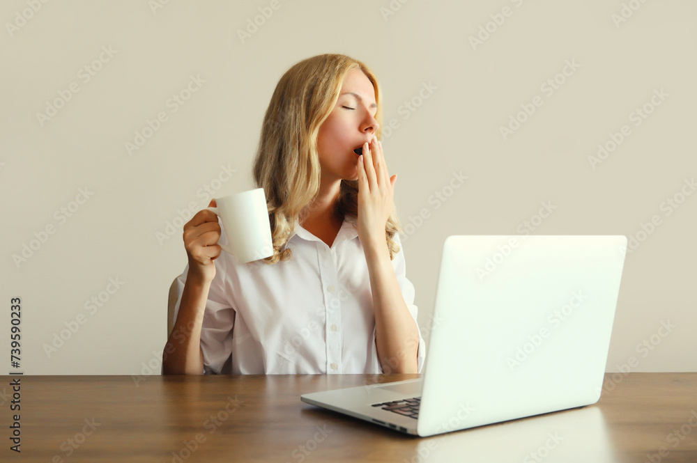 Tired overworked sleeping woman employee yawns, drinks coffee working with laptop in office Tired overworked sleeping woman employee yawns, drinks coffee working with laptop in office