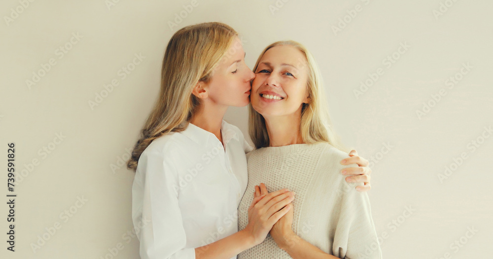 Portrait of adult daughter kissing her happy smiling caucasian middle aged mother