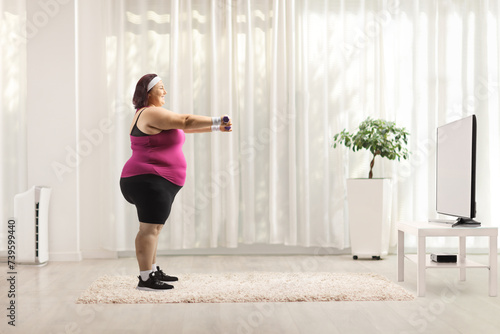 Full length profile shot of a plus size woman exercising with dumbbells