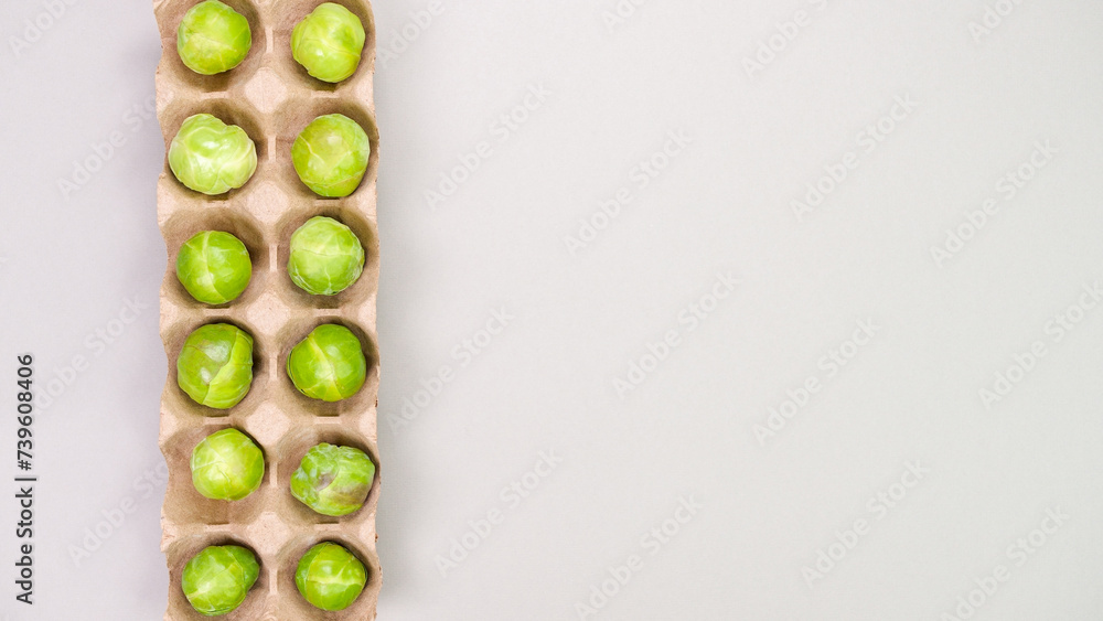 Raw organic Brussel sprouts in brown egg container on grey background, top view. Flat lay, overhead, from above. Copy space. Raw organic Brussel sprouts in brown egg container on grey background, top view. Flat lay, overhead, from above. Copy space.