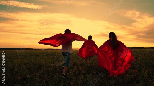 Child imagine being comic book heroes running across meadow in red capes. Children in red capes run across field pretending to be superheroes. Kids actively spend evening dressed as superheroes  dream