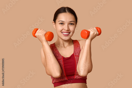 Portrait of young woman in sportswear and with dumbbells on beige background