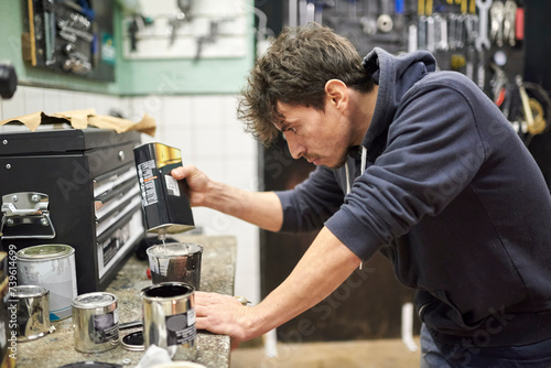 Young hispanic man pouring thinner into a cup of black paint on a workshop countertop. Real people at work. photo