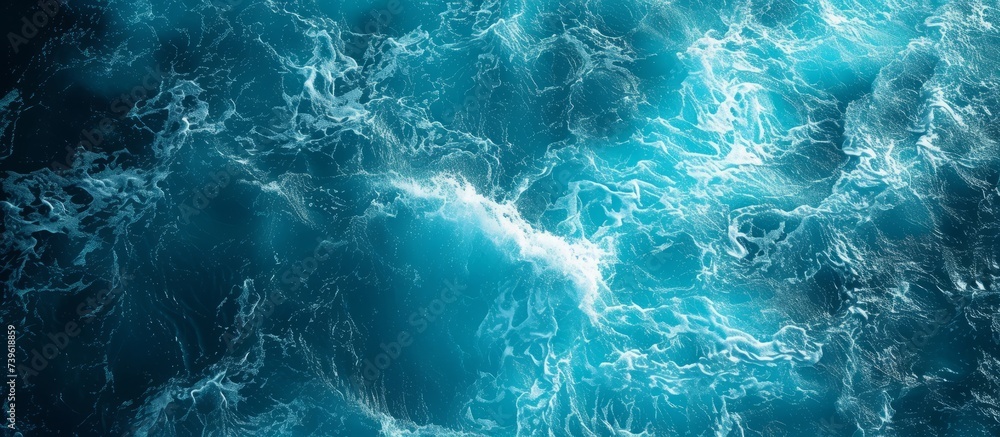 An aerial view of a vast body of fluid, with wind waves creating a pattern on the electric blue water, along with underwater reefs supporting marine biology An aerial view of a vast body of fluid, with wind waves creating a pattern on the electric blue water, along with underwater reefs supporting marine biology