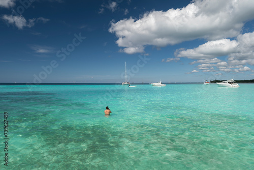 Man swimming in crystal clear shallow turquoise ocean water  deep blue sky and white yacht on the horizon. Saona Island  Dominican Republic. Wide angle shot.