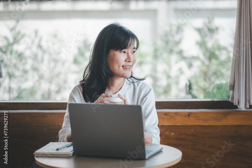 Business freelance concept, A hopeful woman engaging with her laptop in a spacious cafe, with the comfort of natural light from a large window. © Mongta Studio