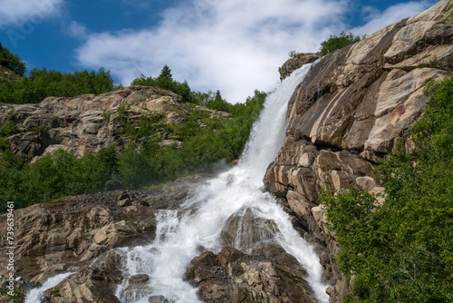View of the Alibek waterfall formed by the fall of the Jalovchatka River from the Alibek glacier on a sunny summer day, Dombay, Karachay-Cherkessia, Russia