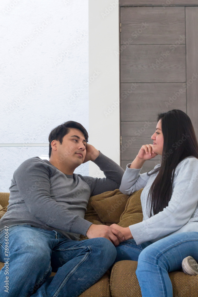 Pareja viéndose fijamente a los ojos mientras se toman de la mano. Matrimonio sentado en el sofá de la sala Pareja viéndose fijamente a los ojos mientras se toman de la mano. Matrimonio sentado en el sofá de la sala