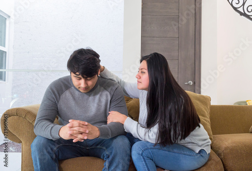 Esposa motivando a su marido tomándolo del brazo. Joven pareja sentada en el sofá de la sala