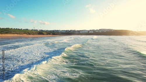 Fistral Beach Surf with Waves Rolling Over Beach. Aerial Drone Tracking Shot with Warm Sunlight. photo