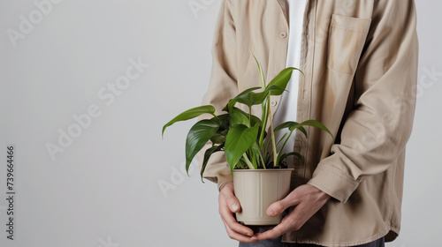 Person in a beige shirt holding a potted green houseplant, with a clear space on the right for text; suitable for themes such as sustainability, growth, or eco-friendly living