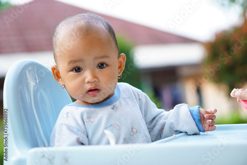 portrait of a cute and adorable Asian baby girl eating while sitting in a baby feeding chair photo