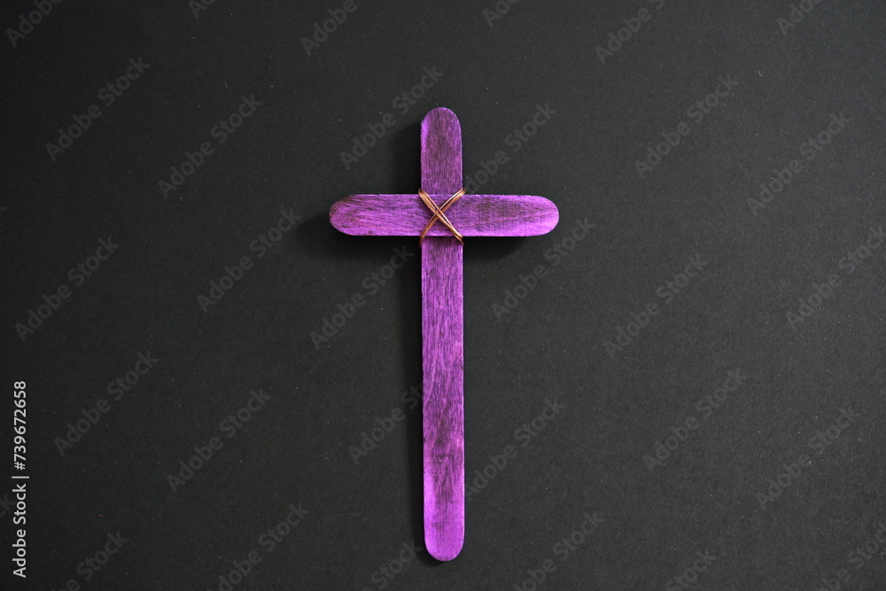 A purple wooden cross in black background. Christian faith, holy week or lent season celebration concept.