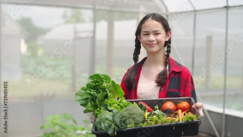Happy teenage girl holding a crate of organic vegetables in greenhouse garden. School student enjoy and fun outdoor lifestyle learning and working with nature healthy food for sustainable living.