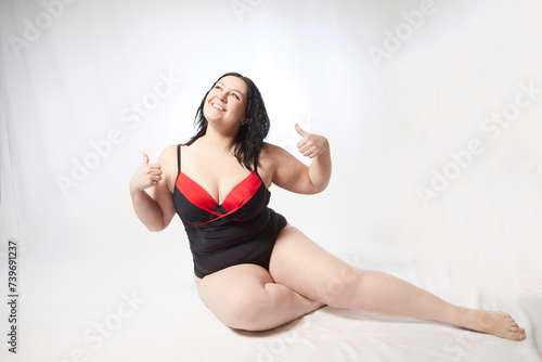 Fototapeta Naklejka Na Ścianę i Meble -  Portrait of attractive dreamy thick woman in red black swimsuit posing on white background. Body positive, photo shoot, selfie. Funny plus size model