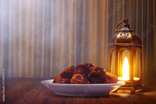 Shiny arabic lantern and bowl of fresh dried dates on wooden floor with golden curtain at night , Ramadan kareem background
