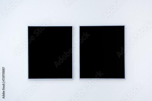 Mockup two blank space in black vertical square artist painting frames, isolated on white wall background. Empty 2 photo frames hanging on white wall in museum.