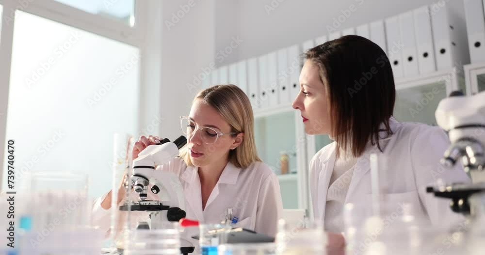 Blonde looks at good results through microscope and smiles Blonde looks at good results through microscope and smiles