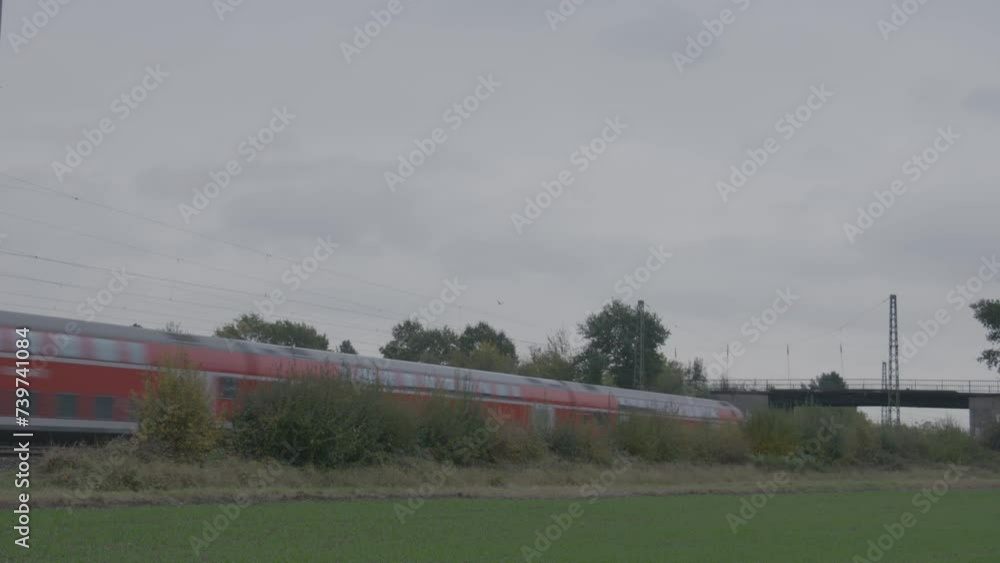Red passenger train in motion on a cloudy day, blurred by speed, with greenery in the foreground Red passenger train in motion on a cloudy day, blurred by speed, with greenery in the foreground
