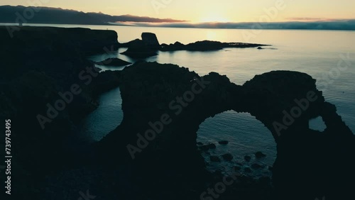 Incredible drone aerial of coral sea arch and coastal lands during sunset.  Gatklettur.  Hellnar Arch Iceland.  The camera moves from right to left. photo