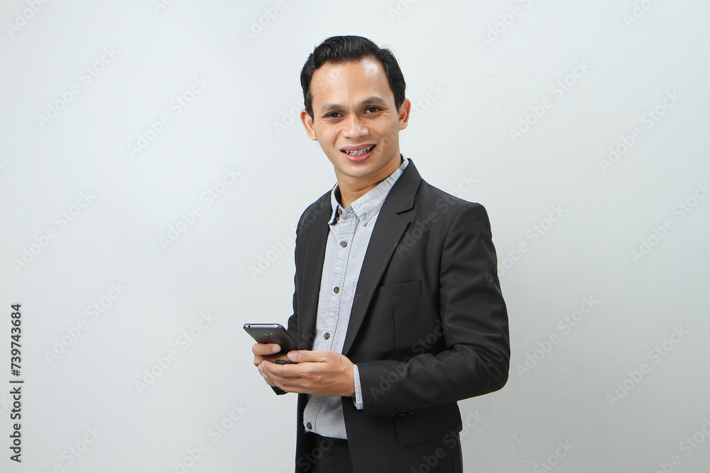 happy asian indonesian business man in suit holding smart phone on isolated background happy asian indonesian business man in suit holding smart phone on isolated background