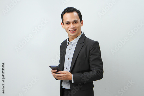 happy asian indonesian business man in suit holding smart phone on isolated background