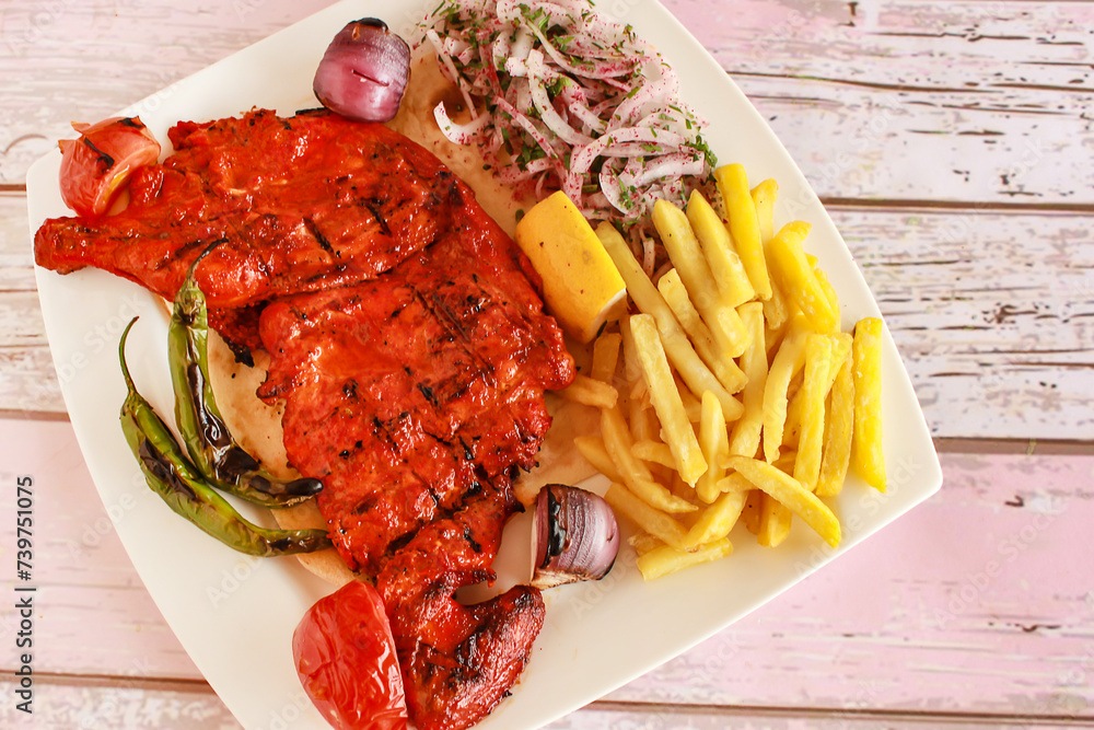 HALF GRILLED TANDOORI CHICKEN with lemon, onion and french fries served in dish isolated wooden table top view of tandoori grill bbq food HALF GRILLED TANDOORI CHICKEN with lemon, onion and french fries served in dish isolated wooden table top view of tandoori grill bbq food
