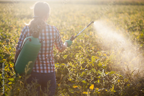 woman in a green backpack with a pressure garden sprayer spraying soybeans against diseases and pests