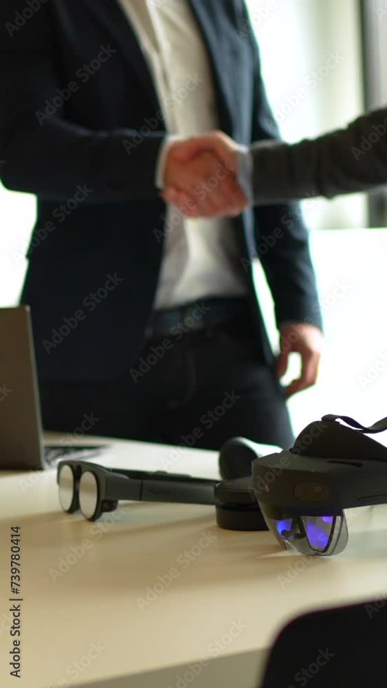 Cropped video of a business hand shake next to laptop and augmented mixed reality goggles Cropped video of a business hand shake next to laptop and augmented mixed reality goggles